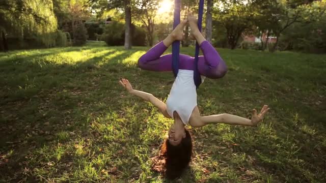 Aerial yoga practitioner stretches herself while suspended on hammock.