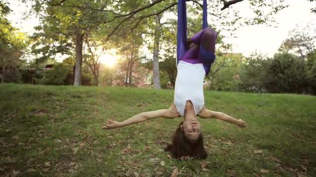 Aerial yoga practitioner stretches herself while suspended on hammock.