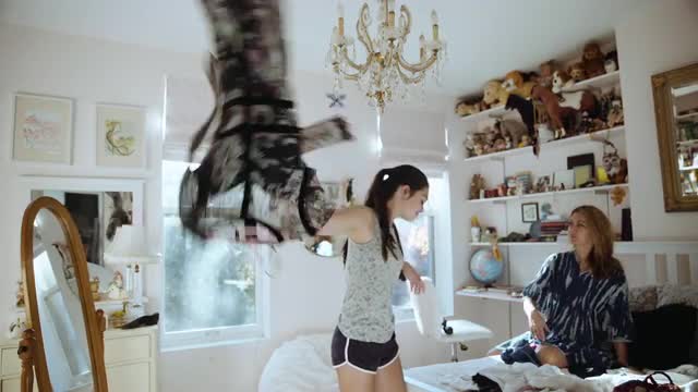 Caucasian girl examining clothing with mother in bedroom