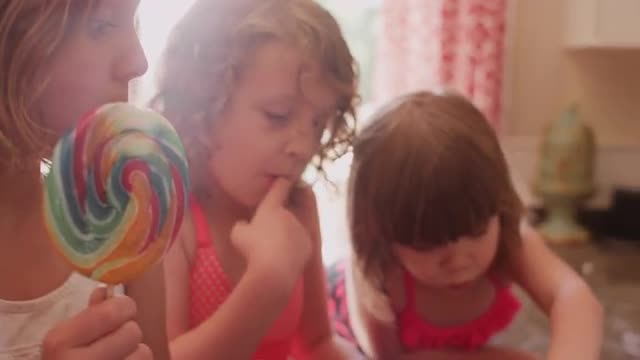 A little girl eating a lollypop and then eating cookie dough with her sisters