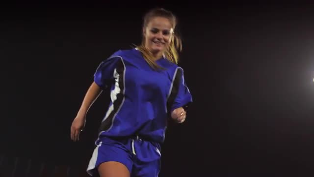 A female soccer player dribbles down the field at night while her opponents slide tackle and defend