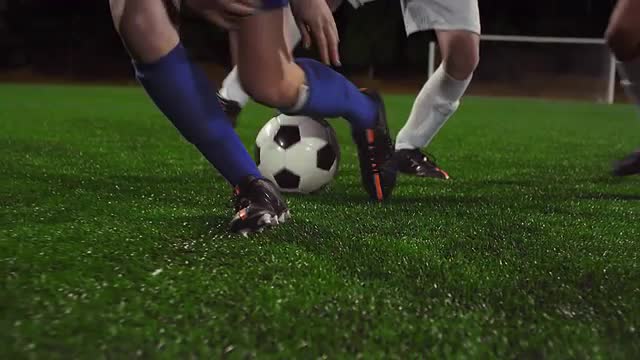 A female soccer player dribbles down the field at night while her opponents slide tackle and defend