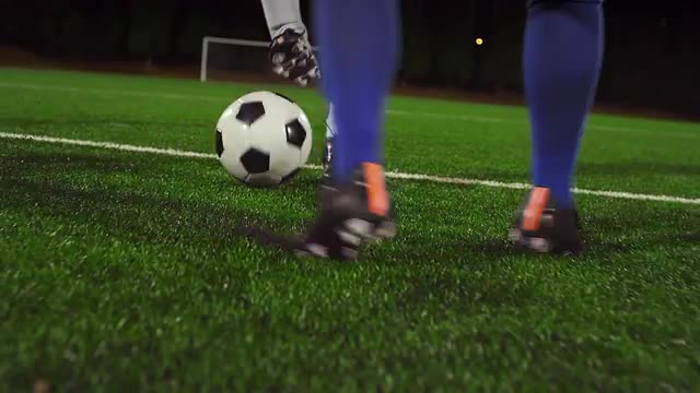 A female soccer player dribbles down the field at night while her opponents slide tackle and defend