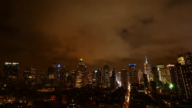 clouds moving over city skyline at night sky. urban building lights background