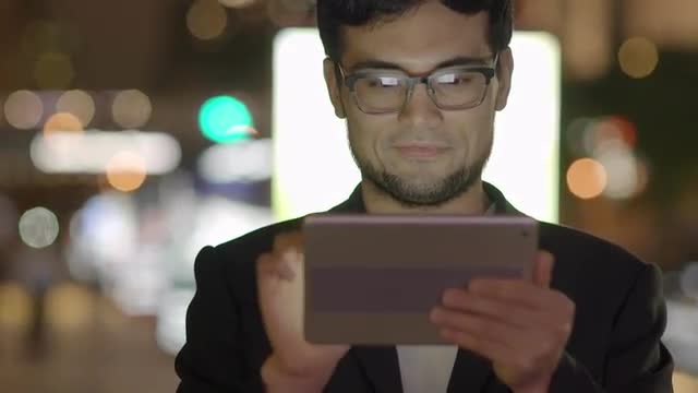 happy young asian man using tablet computer in the city at night