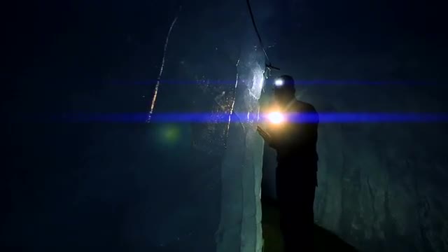 silhouette of male researcher discovering glacier cave holding flashlight