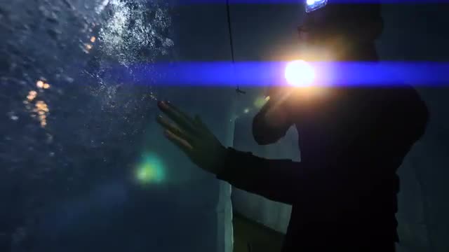 male scientist exploring ice glacier using a flashlight. blue light beam