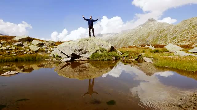 man standing on stone rock raising hands. water reflection. mountain scenery