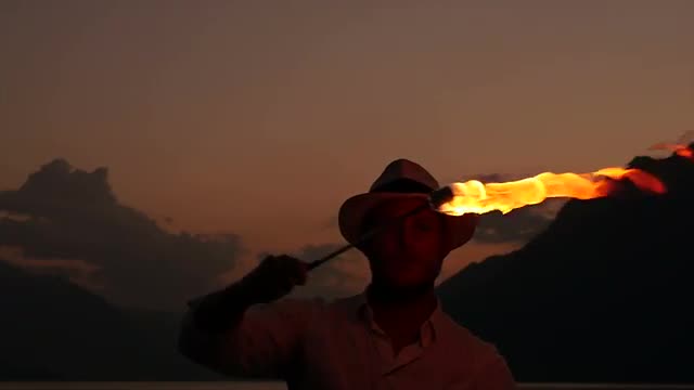 fire artist holding torchlight outdoors in front of lake at night