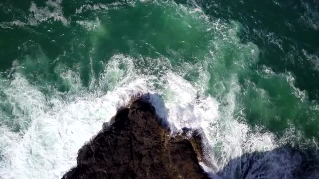 Aerial descending top down view of breaking waves along rocky ocean shore
