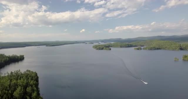 Aerial flying above blue lake with a boat moving down a channel