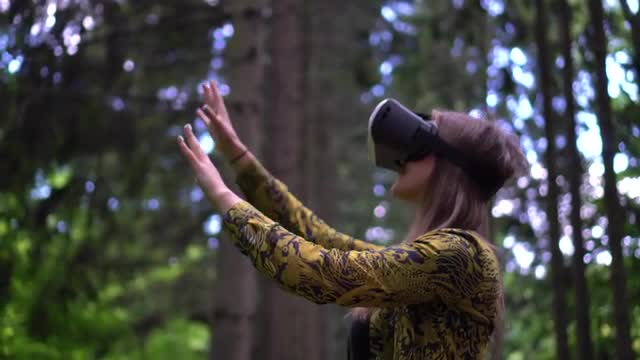 Woman in VR headset looks up at the objects in virtual reality reaching out hands