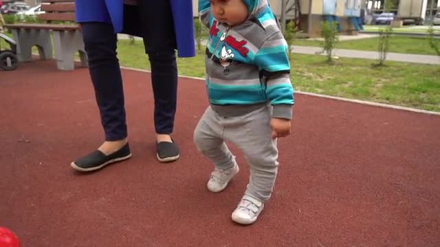Family walks on playground and baby kicks the ball. Slow motion shot