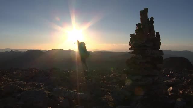 Man walks past rock stack on mountain top