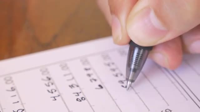 A mans hand adding numbers and writing with a pen on a tax form