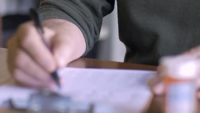 An elderly man puts on his glasses and fills out a medical form on a clipboard