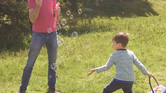 Little boy holding a basket popping bubbles blown by his father