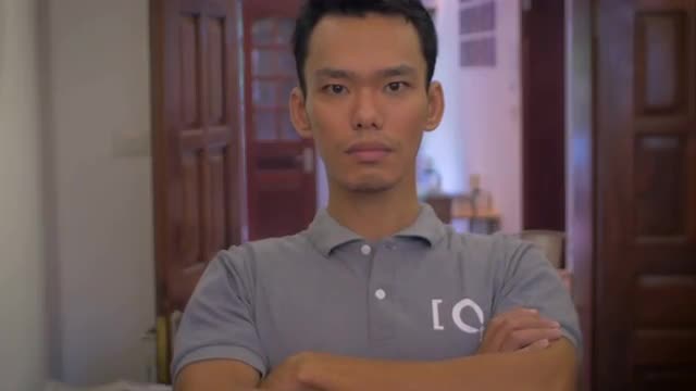 A young Asian man folds his arms and looks directly at the camera