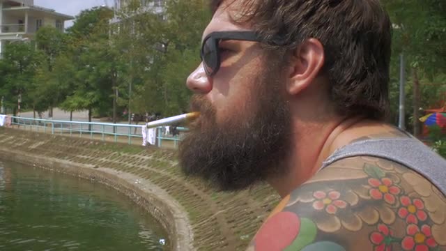 Portrait of a bearded man lighting a cigarette and smoking outside by a lake