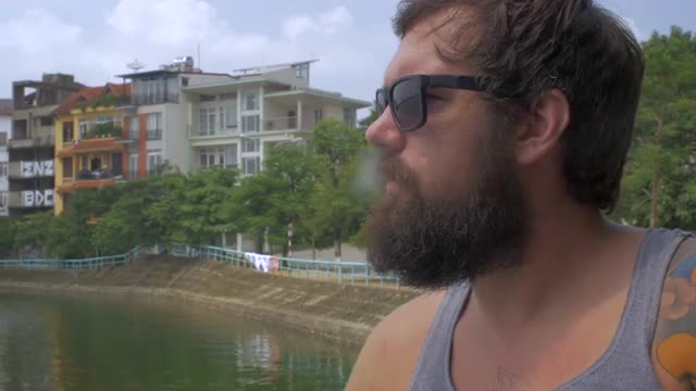 Portrait of a bearded man smoking a cigarette and drinking a beer outside