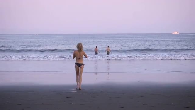 An attractive blond woman runs into the ocean while two men leap over a wave