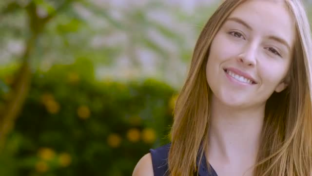 An attractive teen girl model with long hair smiles at the camera - dolly shot