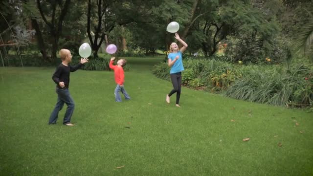 Three cute kids playing together in a park with balloons in slowmo