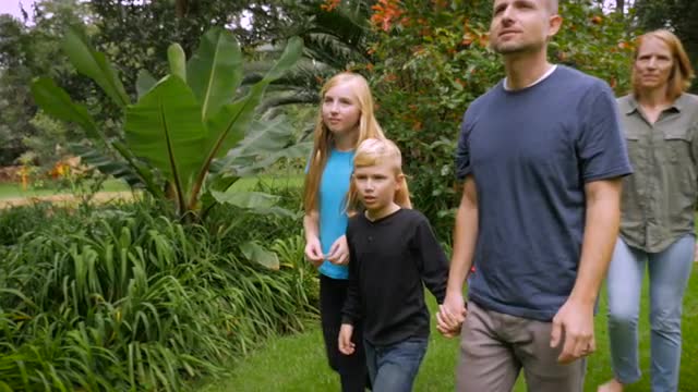 A happy family exploring a tropical garden together while holding hands - slowmo
