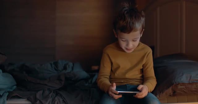 Child with cellphone sitting on bed at home