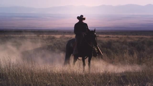 Slow motion static shot of a cowboy riding a horse in a swirl of dust.