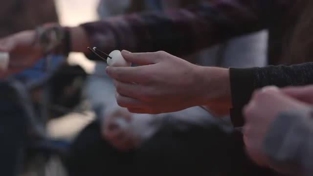 View of people putting marshmallows on roasting sticks