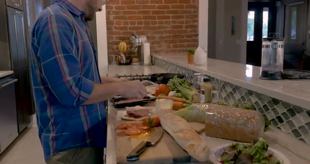 Man making a sandwich with sliced deli meat in his home kitchen
