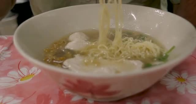 Tilt down of a tourist man eating noodles in soup bowl with chopsticks in Asia