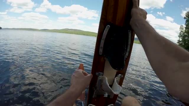 POV of a man putting on vintage wooden water skis on a dock of a lake