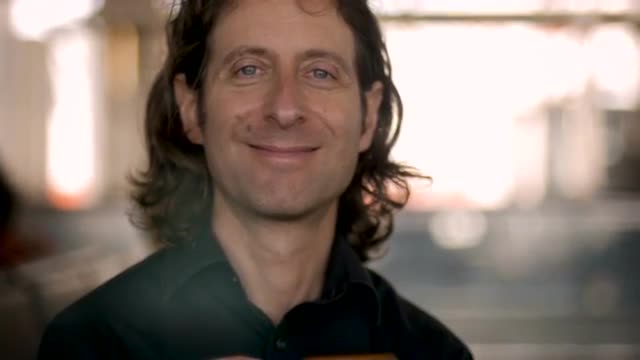 Man in his 30s or 40s using smart phone looks up at camera and smiles