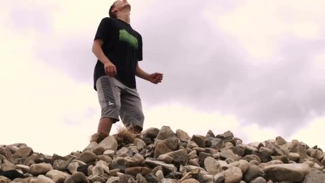 Young man bouncing a soccer ball on his head on a pile of rocks.