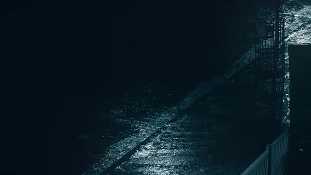 Establishing shot a hard rain falling on pavement at night.
