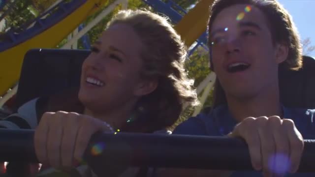 Shot of young couple holding onto safety bar and screaming as coaster goes through loops.