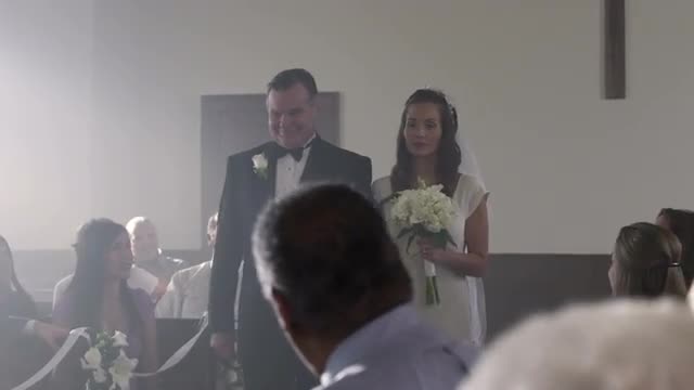 Uncertain looking bride being escorted down the aisle.