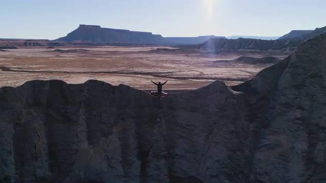 Flying past man with arms in the air at the top of a hill