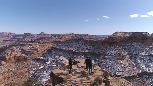 Aerial view flying over 3 people at a view point in the desert