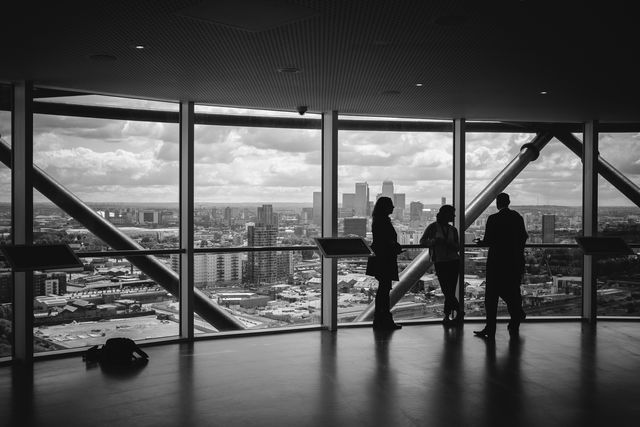 three people standing and talking in an office building looking out large windows