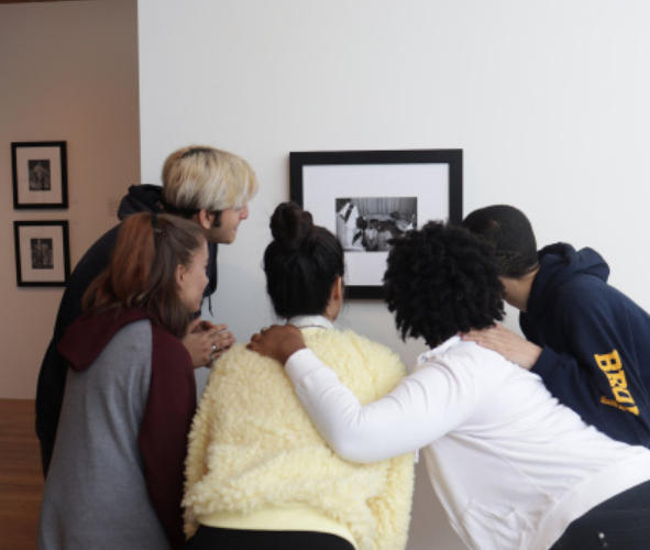Five students huddling around a picture in a gallery