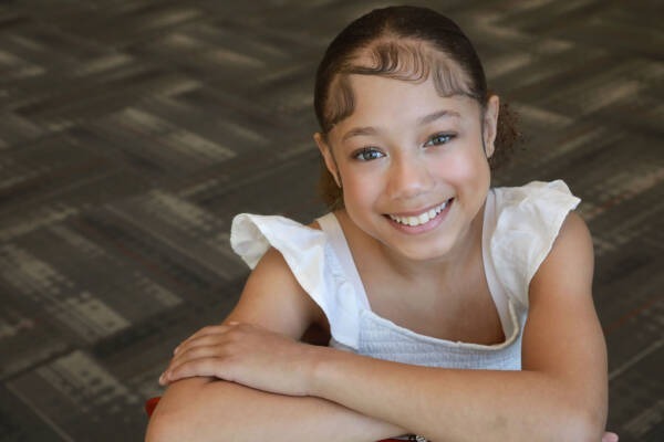A young child smiling with her arms crossed AI-generated content may be incorrect.