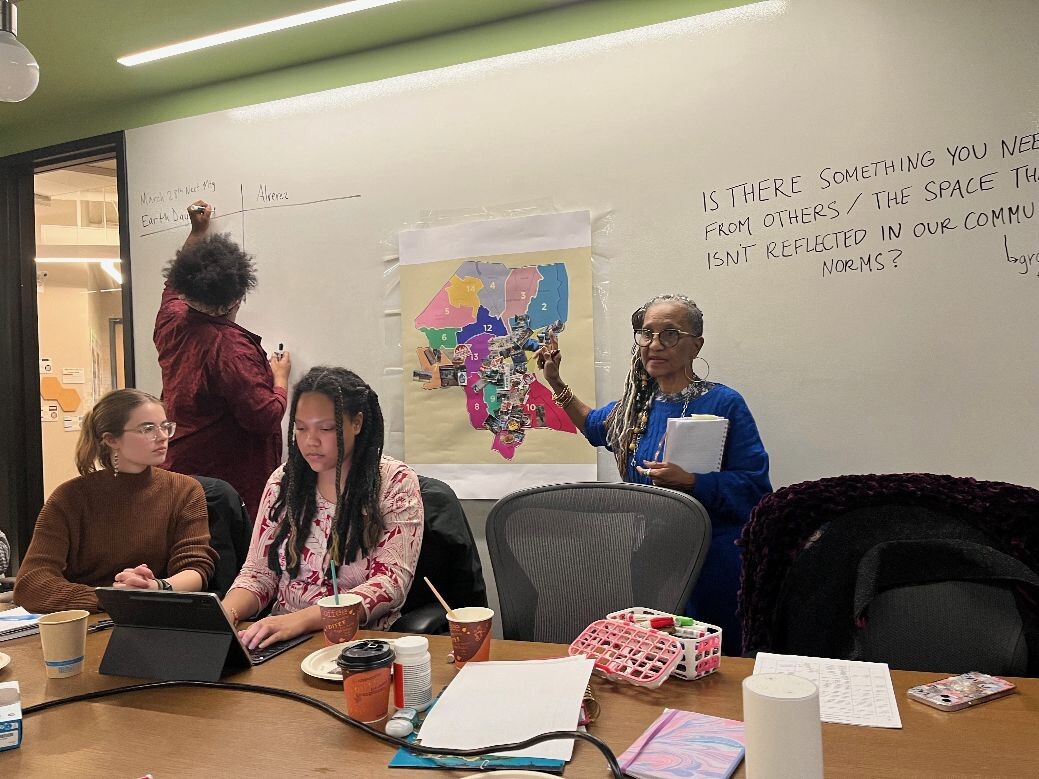 Image of four co-facilitators taking notes and talking to the group while pointing to the Smellage which is taped to the whiteboard behind them.