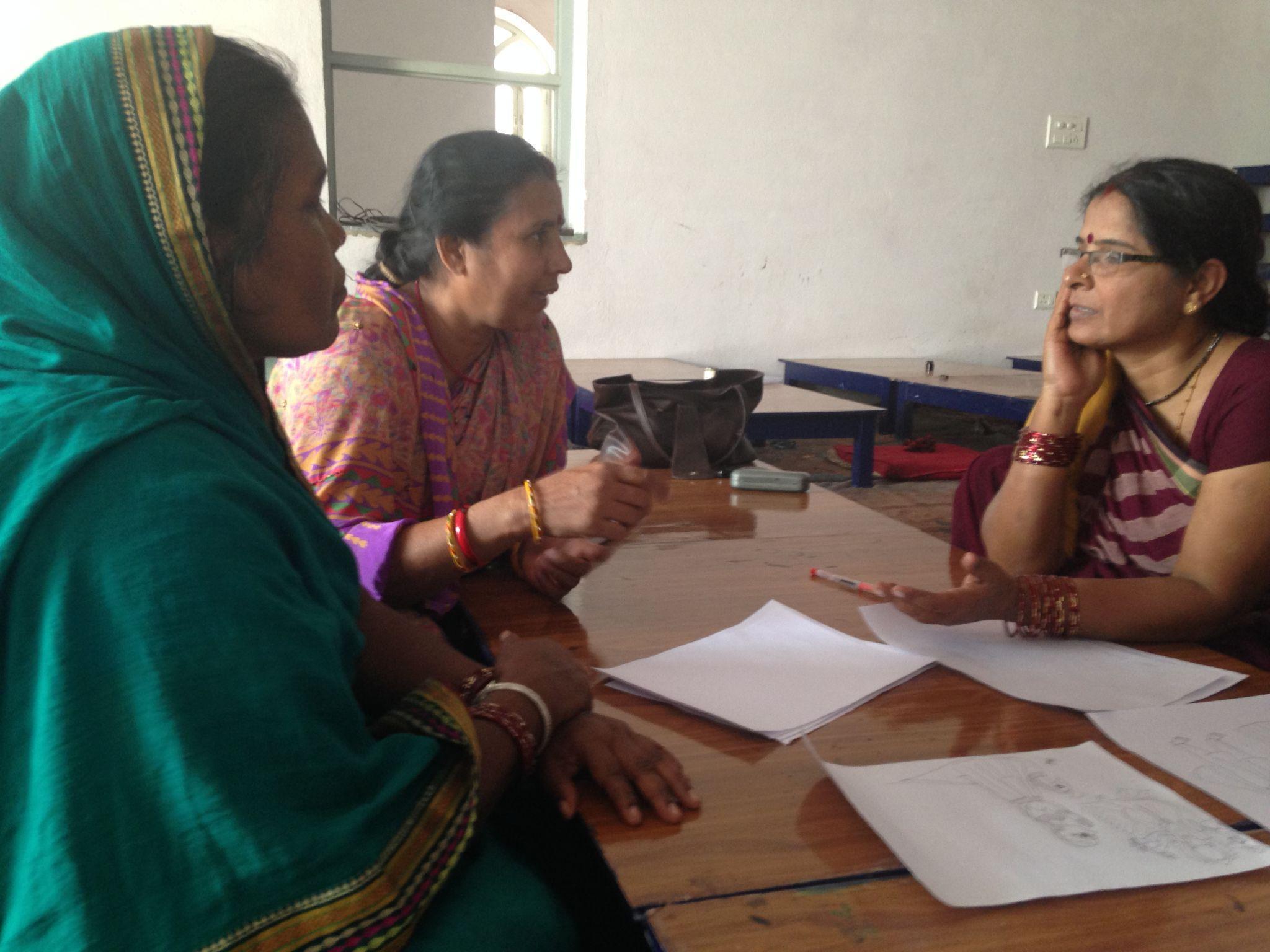 Women sitting at a table talking to a group of women AI-generated content may be incorrect.