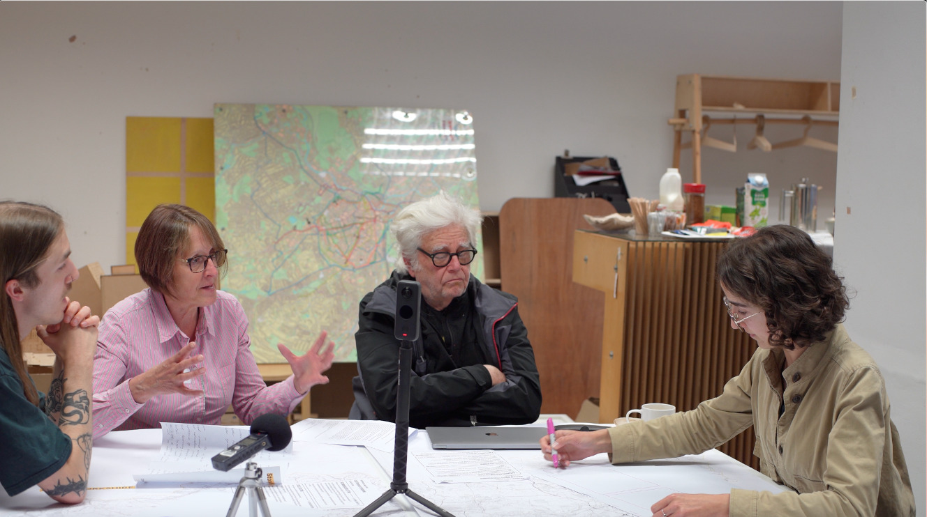 Photograph showing four people sat around a table talking, with one person drawing.