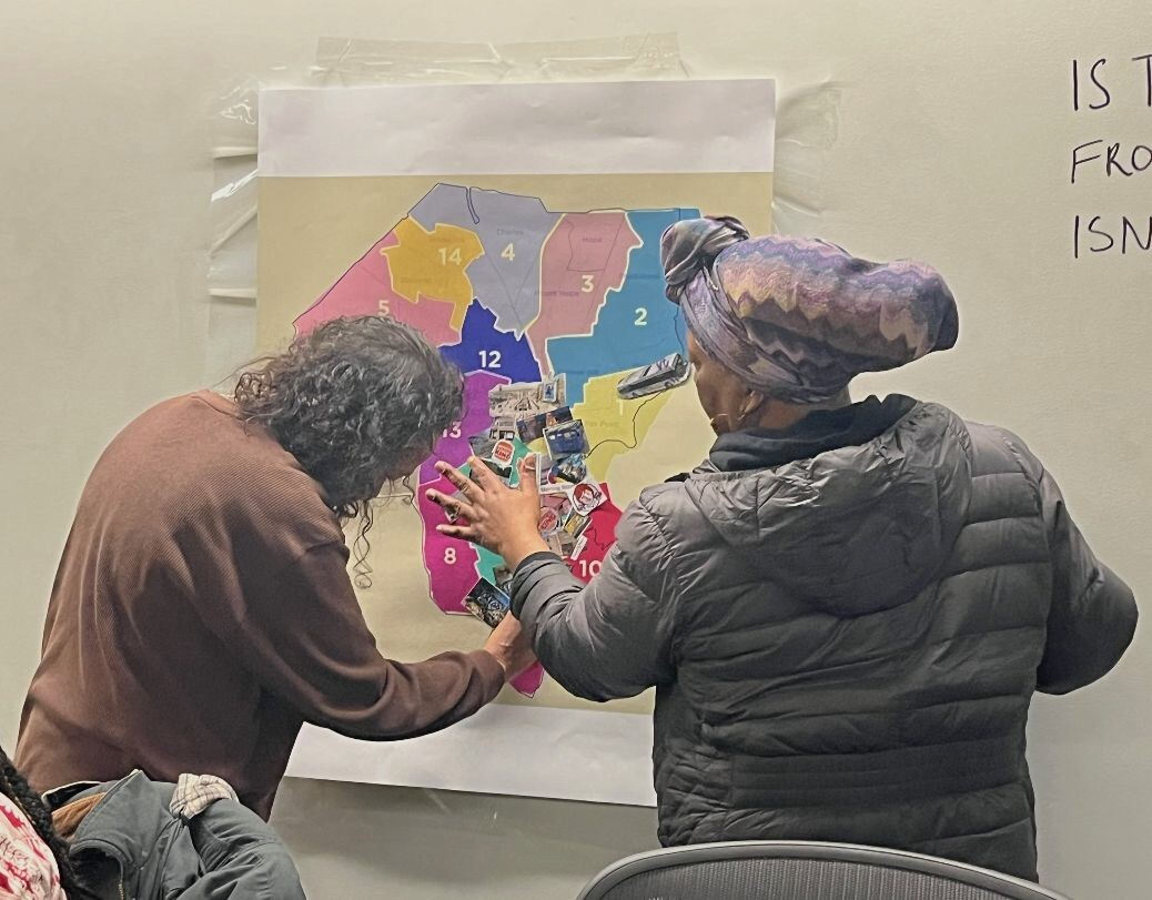Two community researchers in animated discussion while working on and looking closely at the collage.