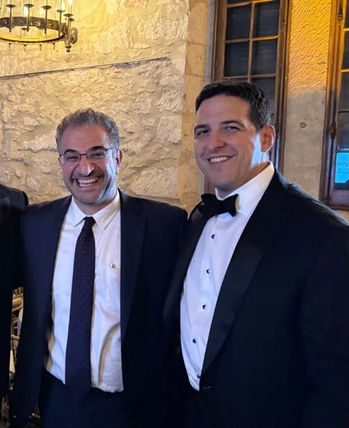 Two men in suits smiling Description automatically generated