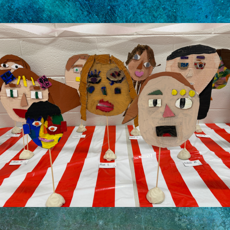 A collection of colorful, handmade cardboard masks with unique facial features displayed on sticks.